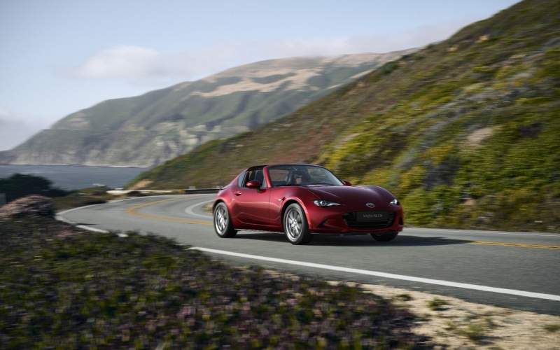 MX-5 rojo, descapotable, siendo conducido por una carretera costera.